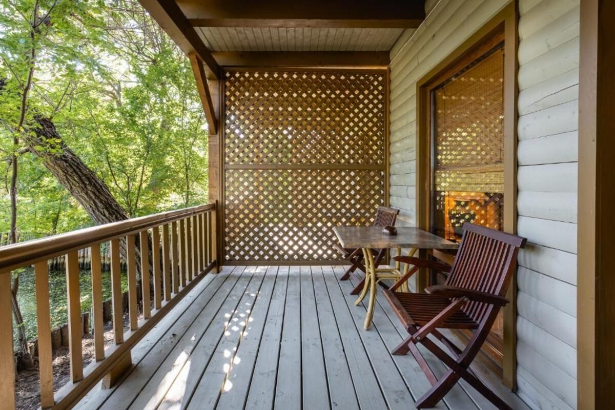 A wooden deck with a table and chairs, surrounded by a lattice fence, overlooking a forested area.