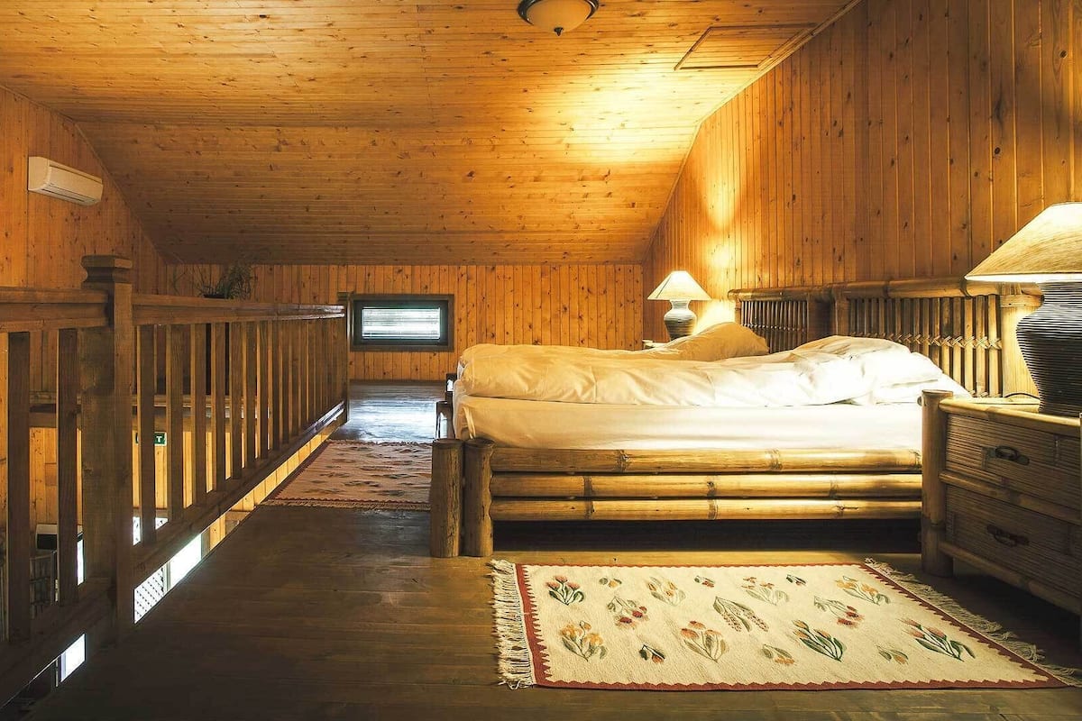 Ein Schlafzimmer einer Holzhütte mit Bett, Nachttisch, Lampe, Fenster und Fernseher.