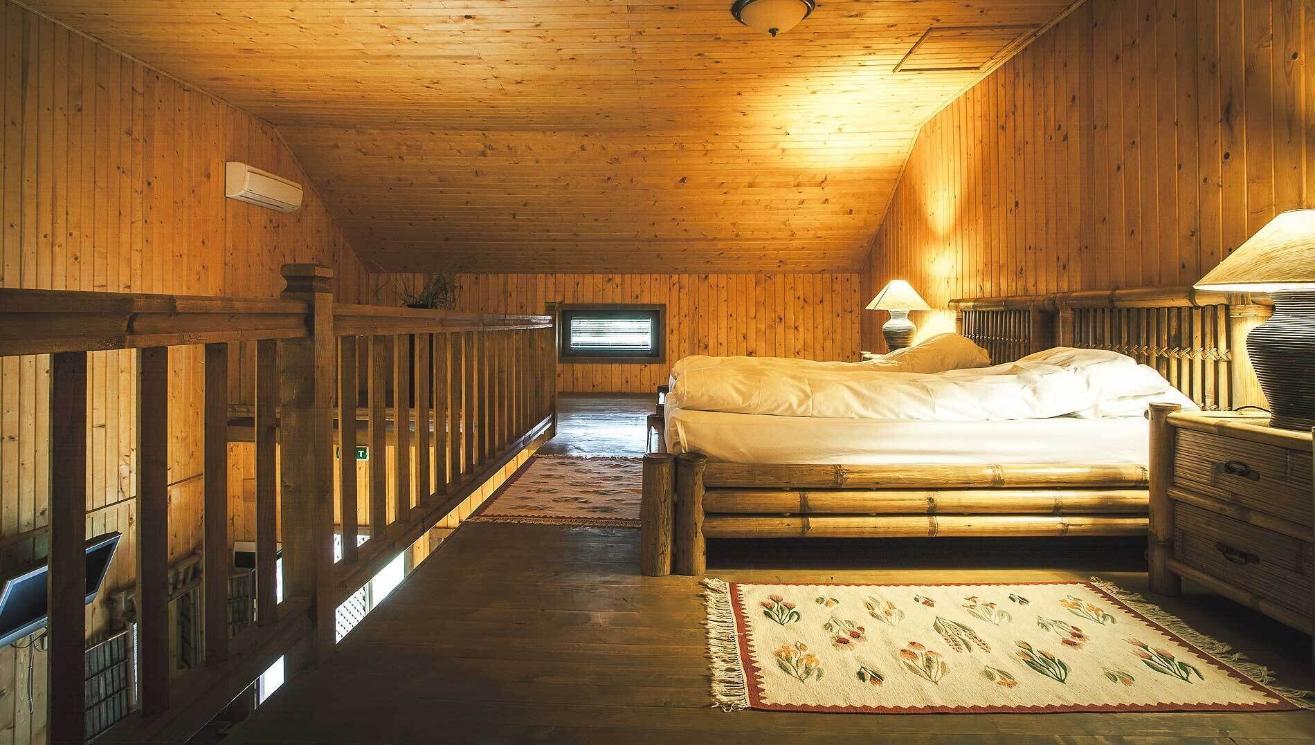 A wooden room with a bed, a lamp, a television, and a window.