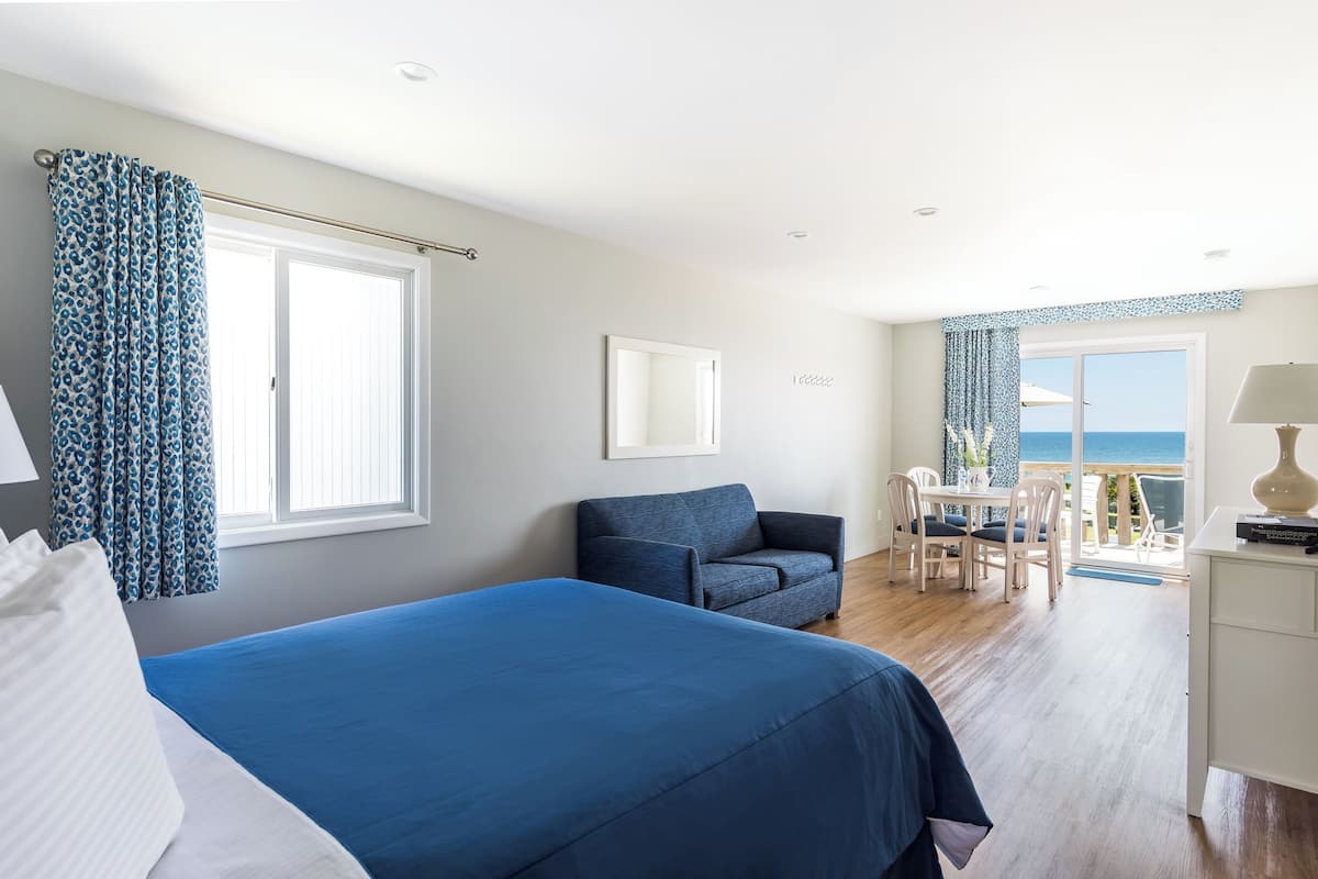 A bedroom with a large bed, a chair, a desk, and a view of the sea.