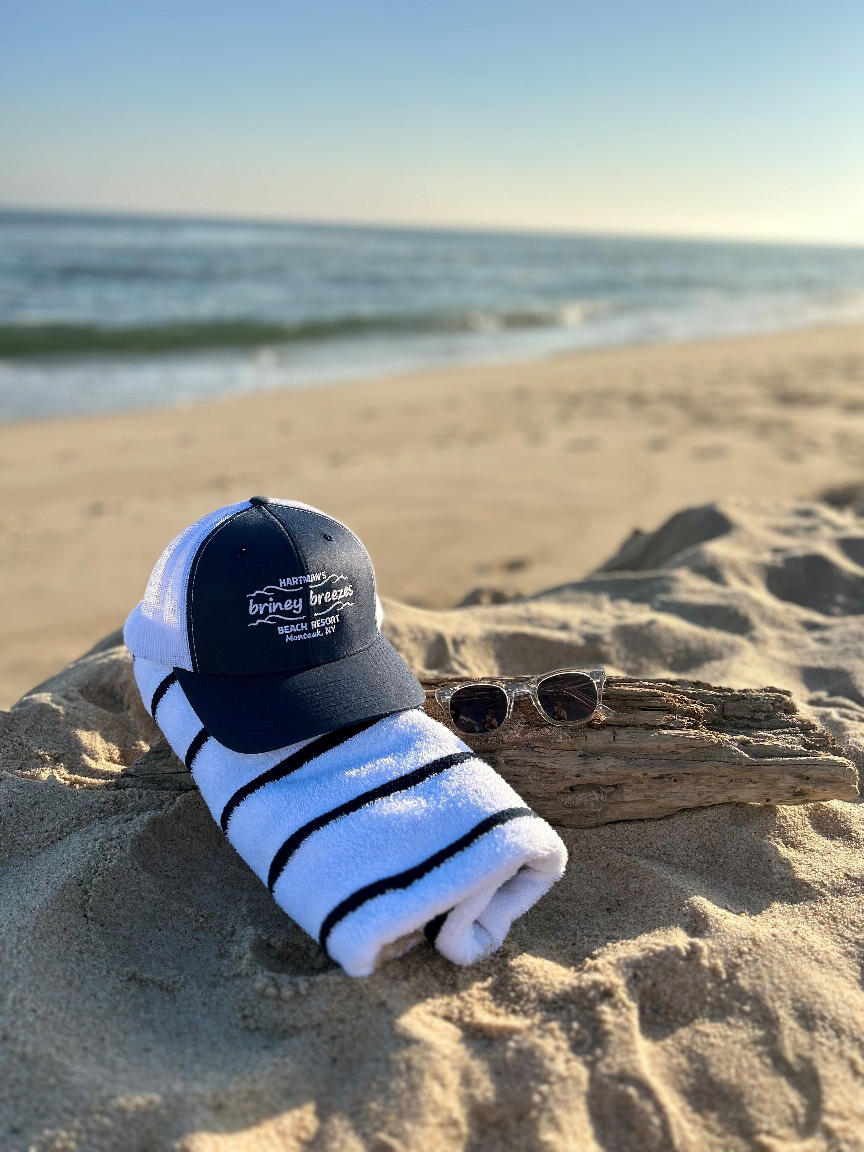 A beach towel and a cap on the sand with a wooden log nearby.