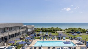 A pool area with lounge chairs and umbrellas, a view of the ocean, and a building with balconies. - Hartmans' Briney Breezes Beach Resort (Montauk)
