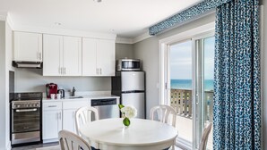 A modern kitchen with white cabinets, a stainless steel stove, a microwave, and a dishwasher. There is a round table with chairs and a vase with flowers. The room has a large sliding glass door leading to a balcony with a view of the ocean. - Hartmans' Briney Breezes Beach Resort (Montauk)
