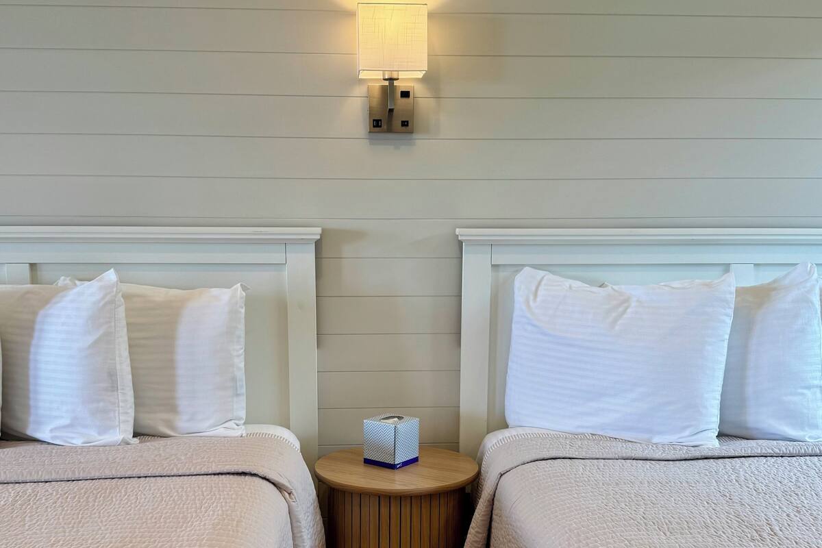 A hotel room with two beds, a small wooden nightstand, and a wall-mounted light fixture.