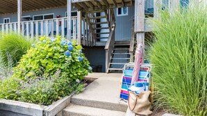 A wooden staircase leading to a building with a blue door, surrounded by lush greenery and a colorful striped bag on the steps. - Hartmans' Briney Breezes Beach Resort (Montauk)