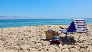 A beach with a chair and a basket on the sand, a clear blue sky, and the ocean in the background. - Hartmans' Briney Breezes Beach Resort (Montauk)