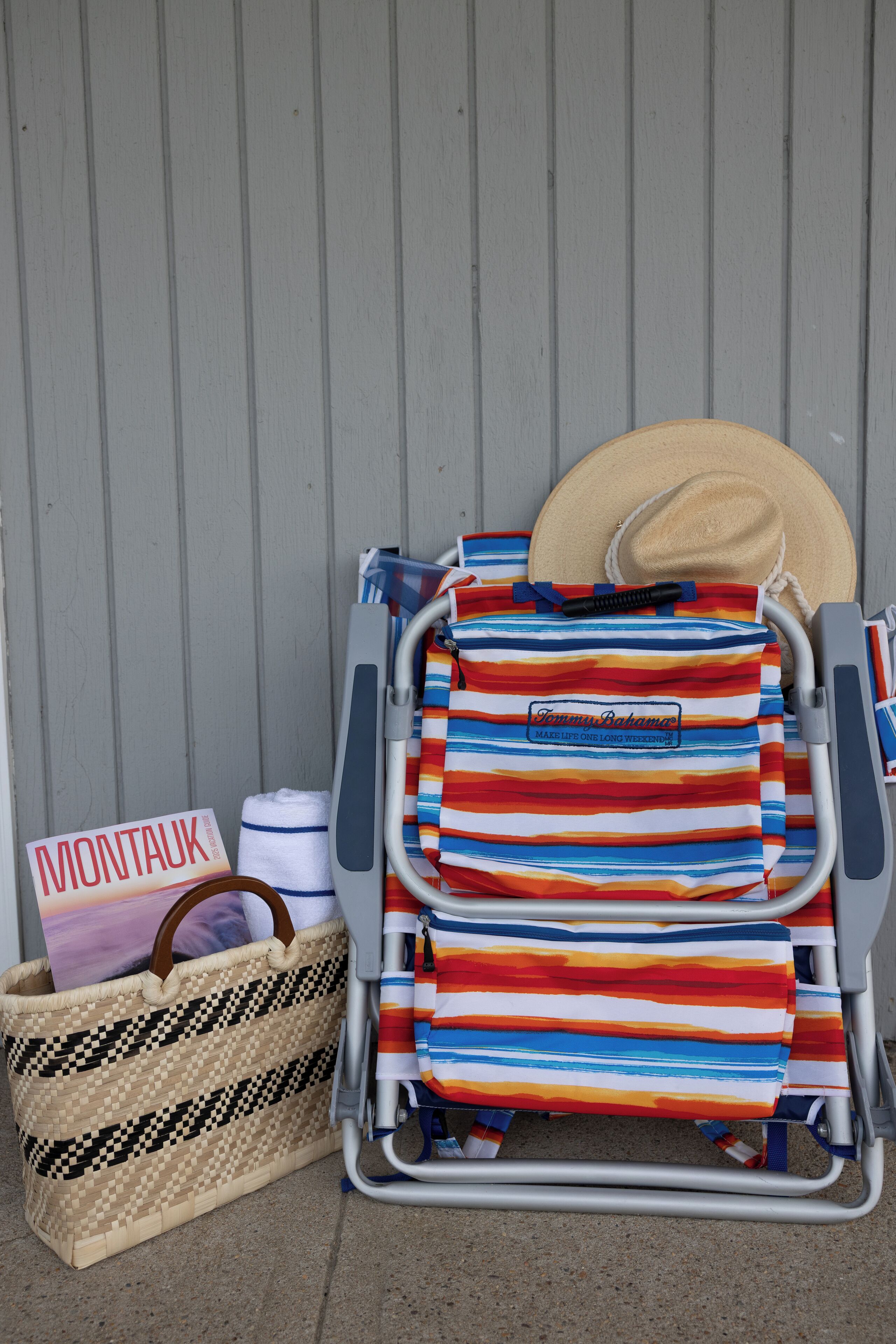 A beach chair with a striped towel, a straw bag, and a magazine titled 'MONTAUK'.