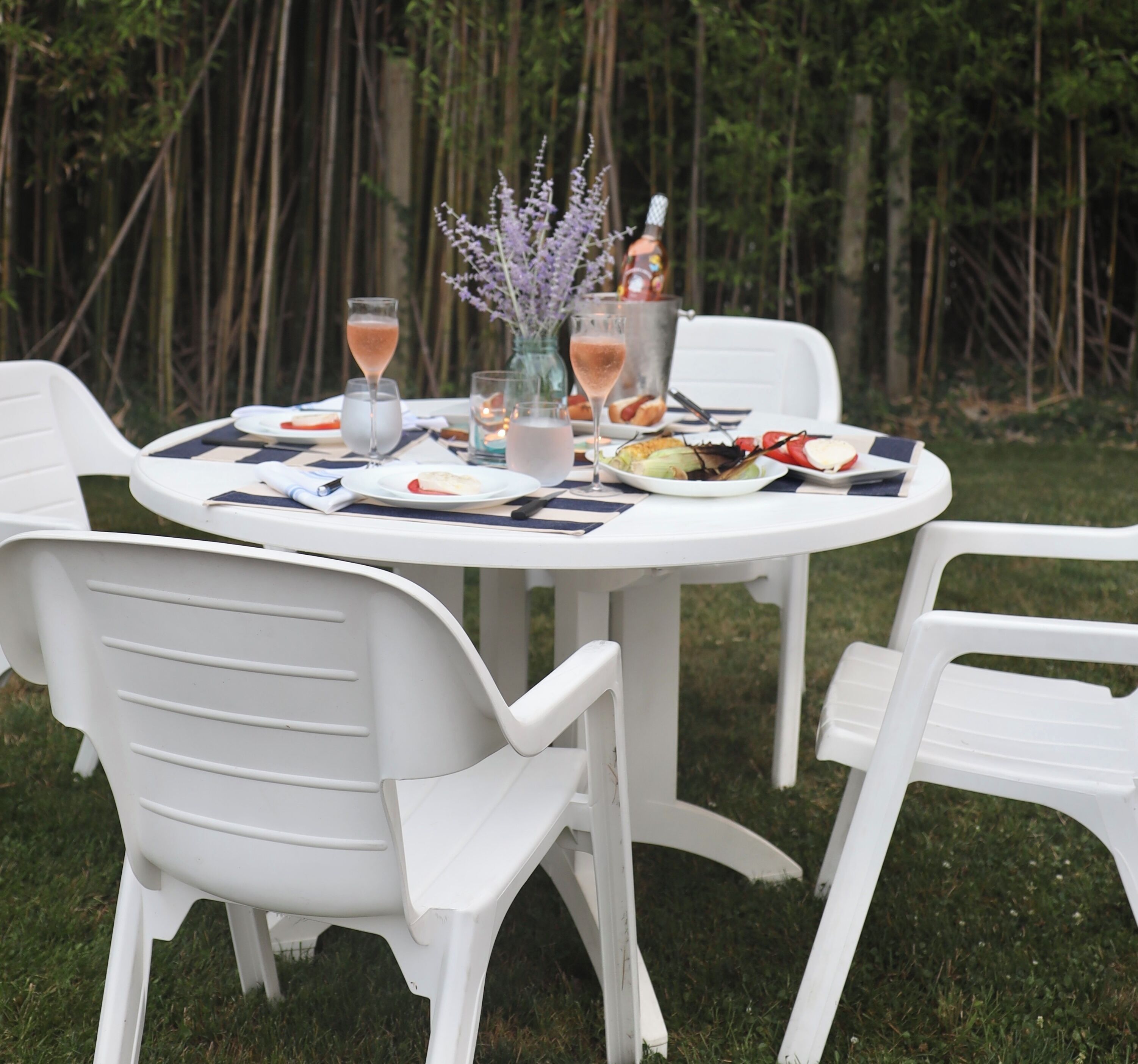 A round white table set outdoors with chairs, surrounded by greenery.