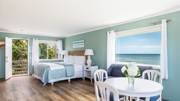 A room with a bed, a table with chairs, a window with a view of the ocean, and a door leading to an outdoor area. - Hartmans' Briney Breezes Beach Resort (Montauk)