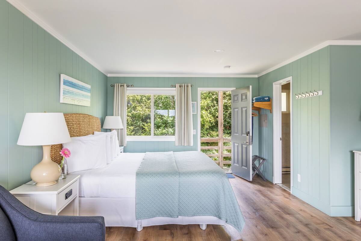 A bedroom with a bed, bedside tables, a lamp, and a view of the outdoors.