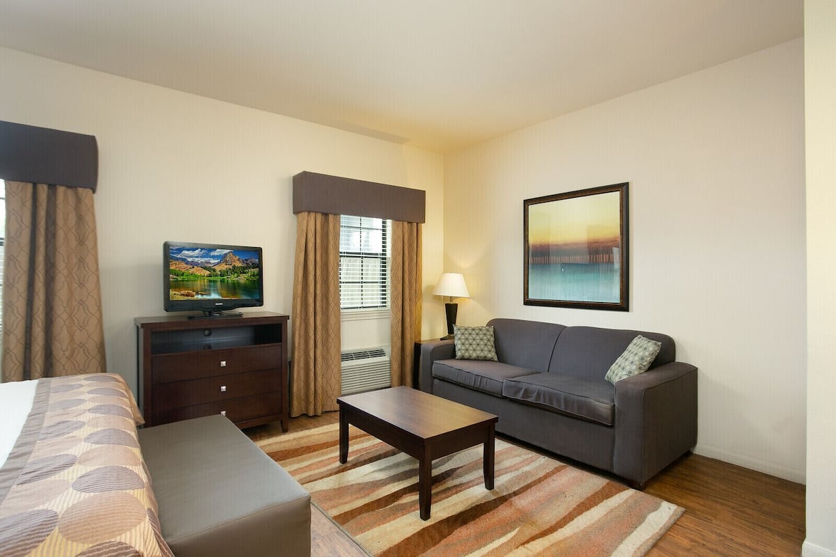 A hotel room with a bed, a sofa, a TV, a desk, and a painting.