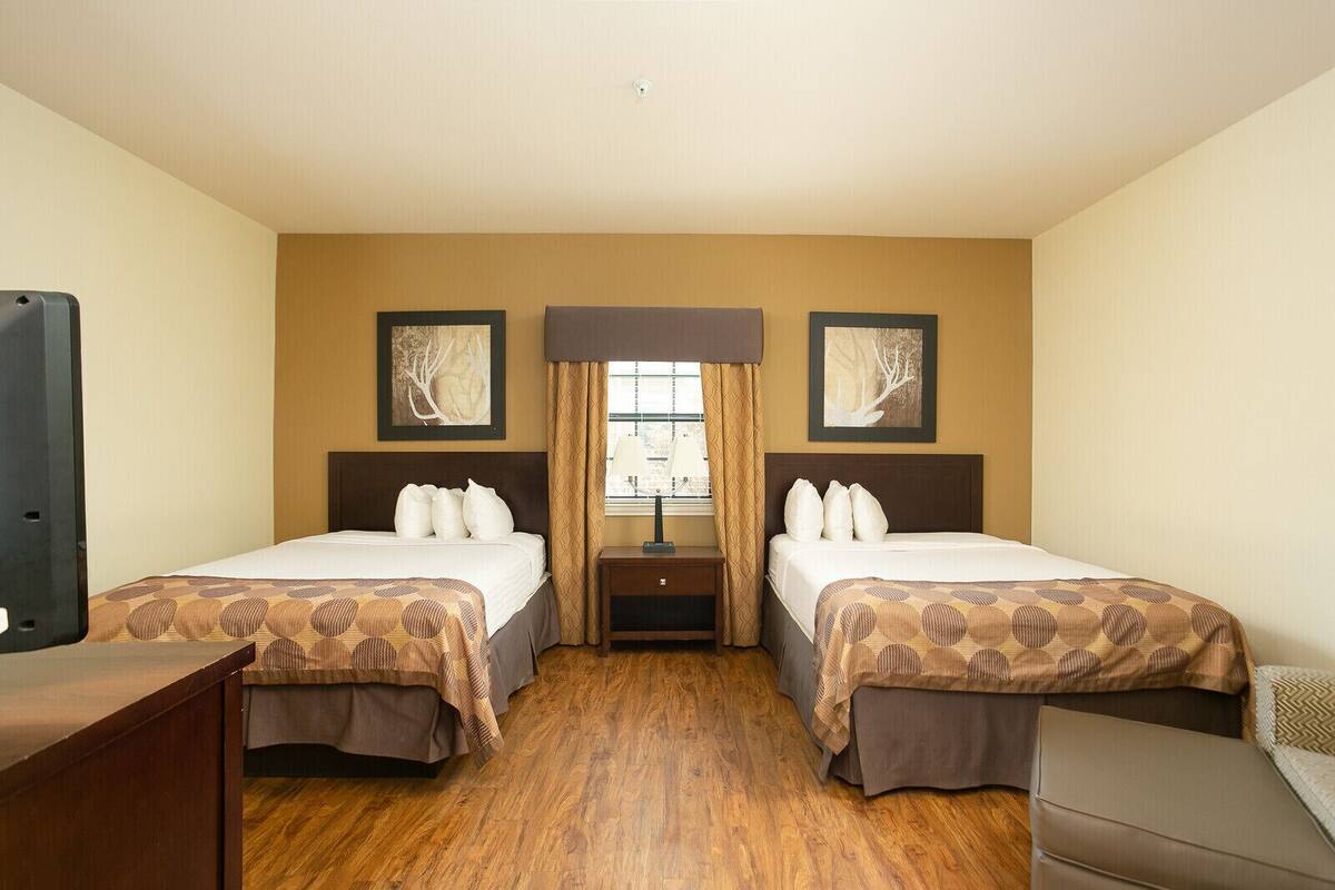 A hotel room with two beds, a desk, and a TV.