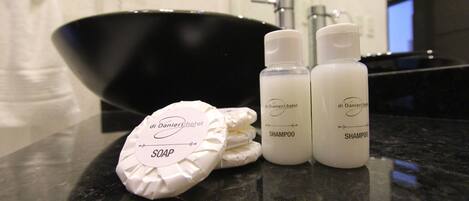 A bathroom counter with a black basin, two bottles of shampoo, and a soap bar with a label.