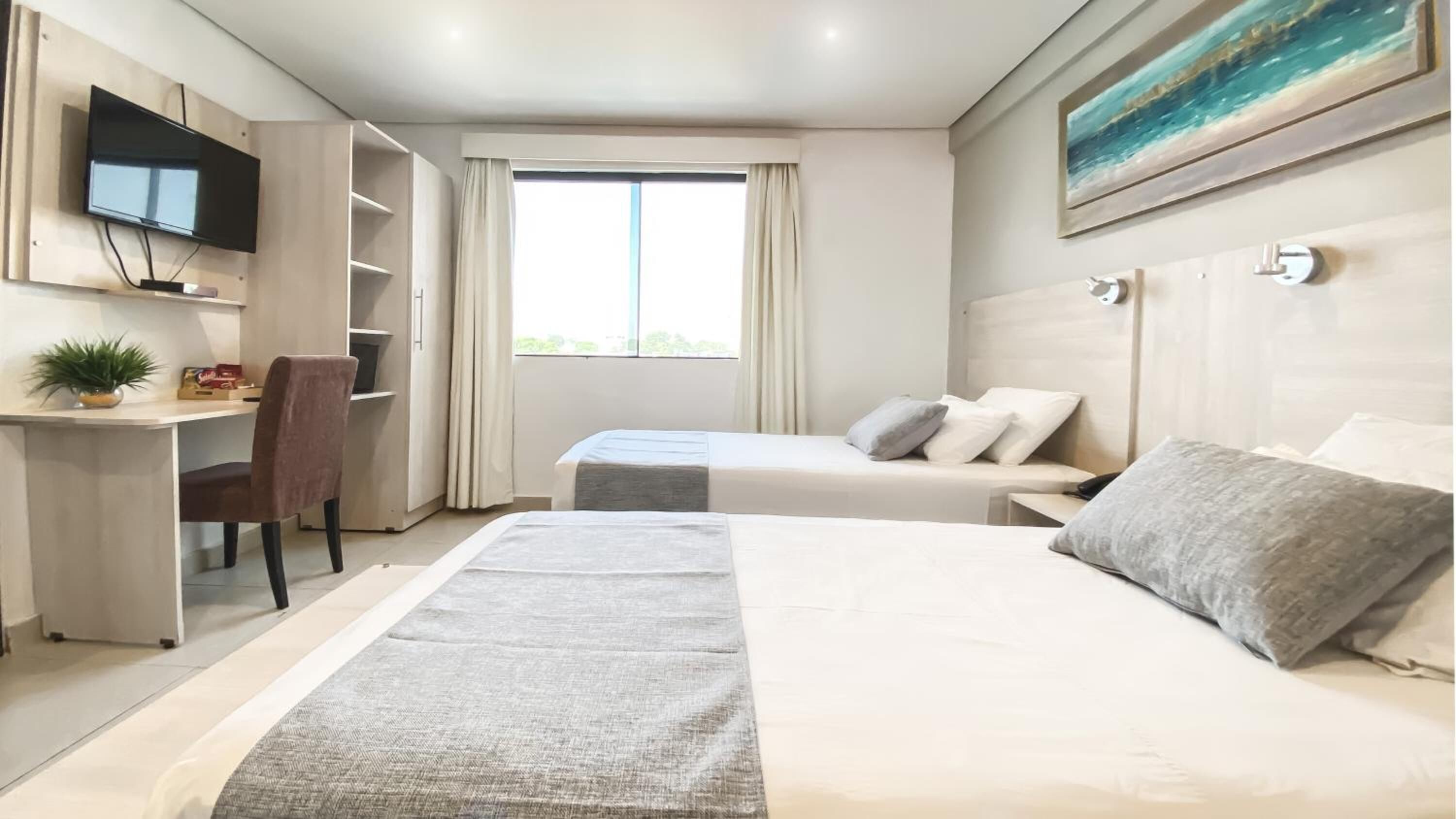 A hotel room with two beds, a desk, a chair, a TV, and a window with curtains.