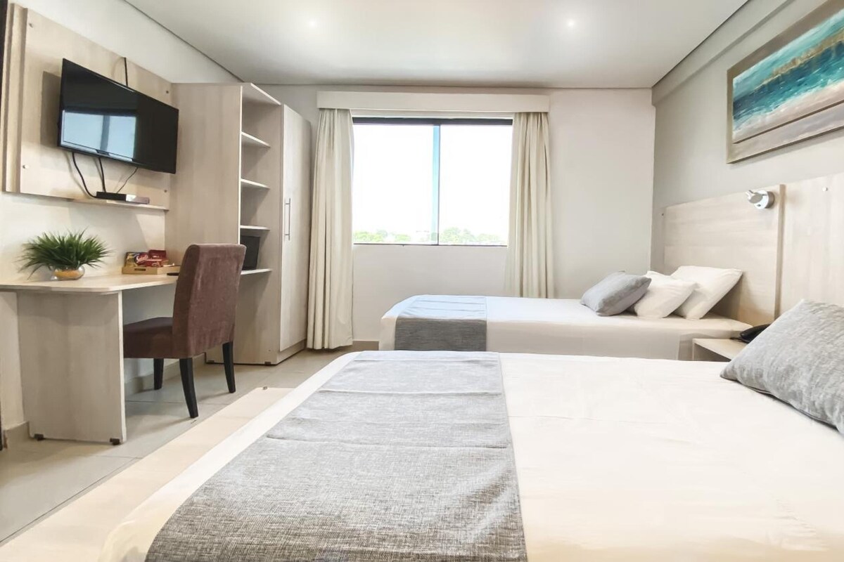 Hotellihuone, jossa on kaksi sänkyä, työpöytä, tuoli, televisio ja ikkuna, jossa on verhot.