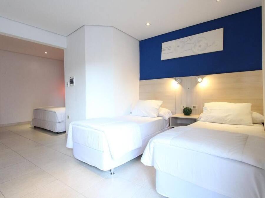 Habitación de hotel con dos camas, una pared de acento azul y un techo blanco.
