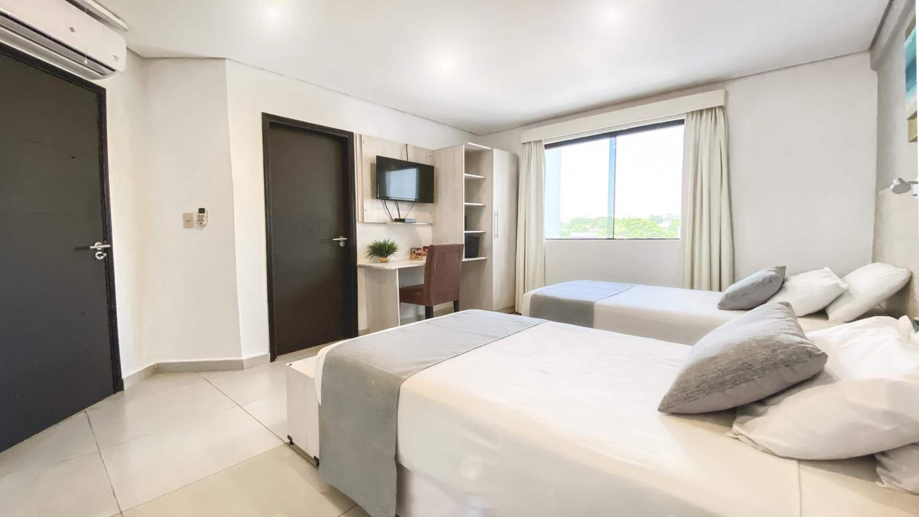 A modern hotel room with two beds, a desk, a TV, and a window with curtains.