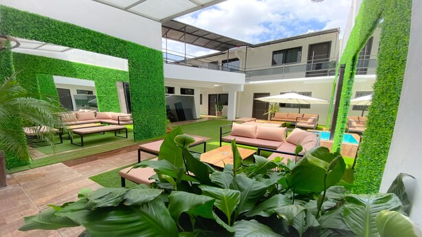 A modern outdoor lounge area with green walls, multiple seating arrangements, and a pool. - Danieri Asunción Hotel (Asunción)