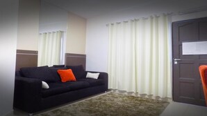 A room with a dark-colored sofa, a white pillow, a rug, and a door with a notice on it. - Danieri Asunción Hotel (Asunción)