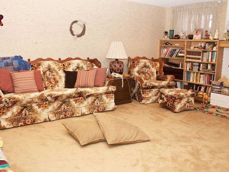 A living room with a floral sofa, a wooden bookshelf, and a fireplace.