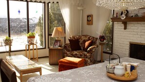 A cozy living room with a fireplace, a dining table, and a view of a snowy landscape through large windows. - Cozy Nest B&B (Calgary)