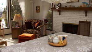 A cozy living room with a fireplace, a floral armchair, and a dining table set with a tray of items. - Cozy Nest B&B (Calgary)