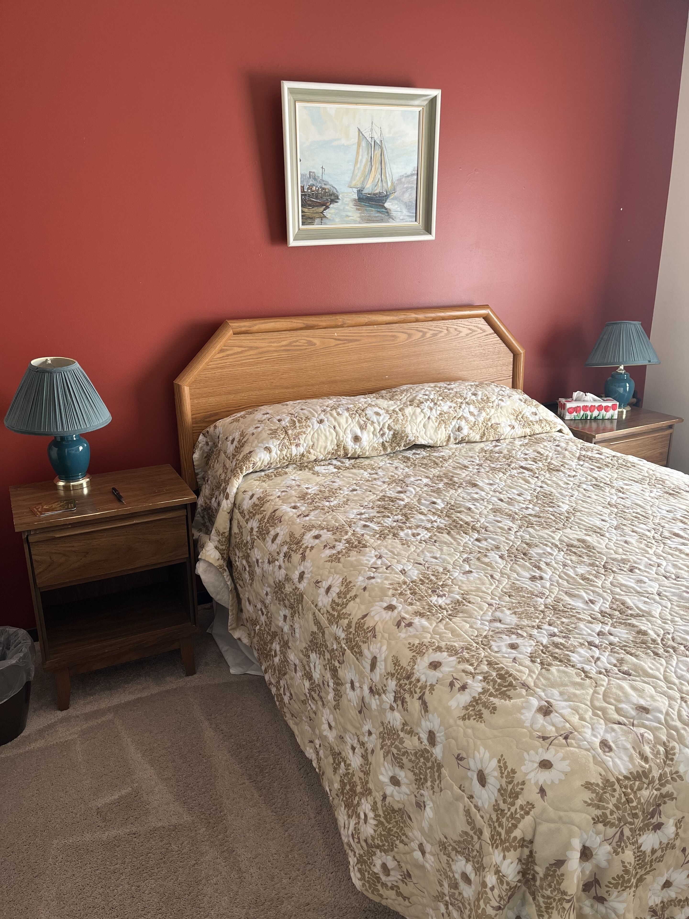 Un dormitorio con una cama de madera, ropa de cama floral, un cuadro de un barco en la pared y dos lámparas de noche.