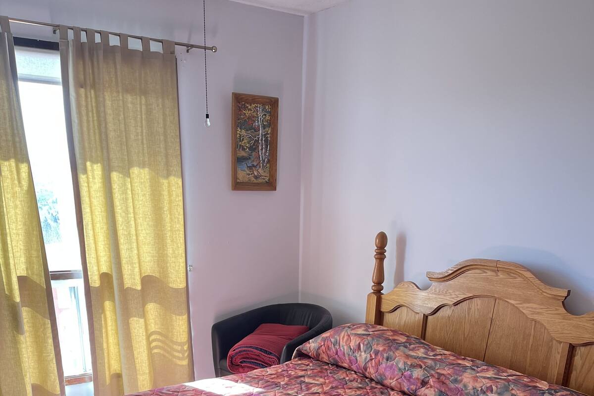 A bedroom with a large bed, a chair, a painting on the wall, and a window with curtains.