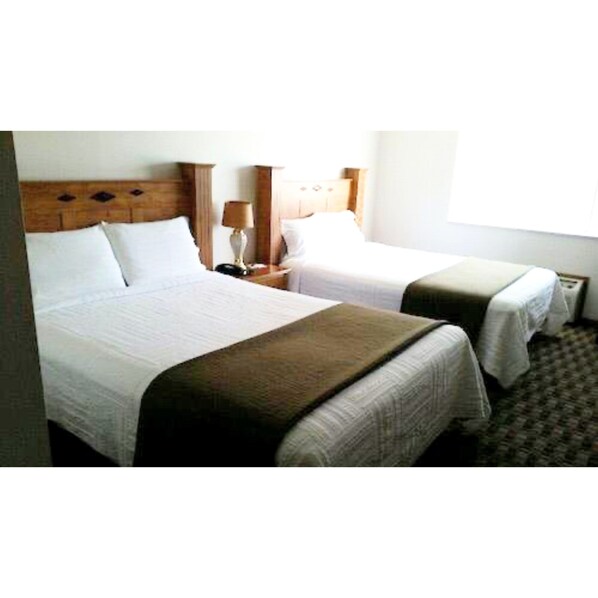 Two single beds with wooden headboards, white linens, and a bedside table with a lamp.