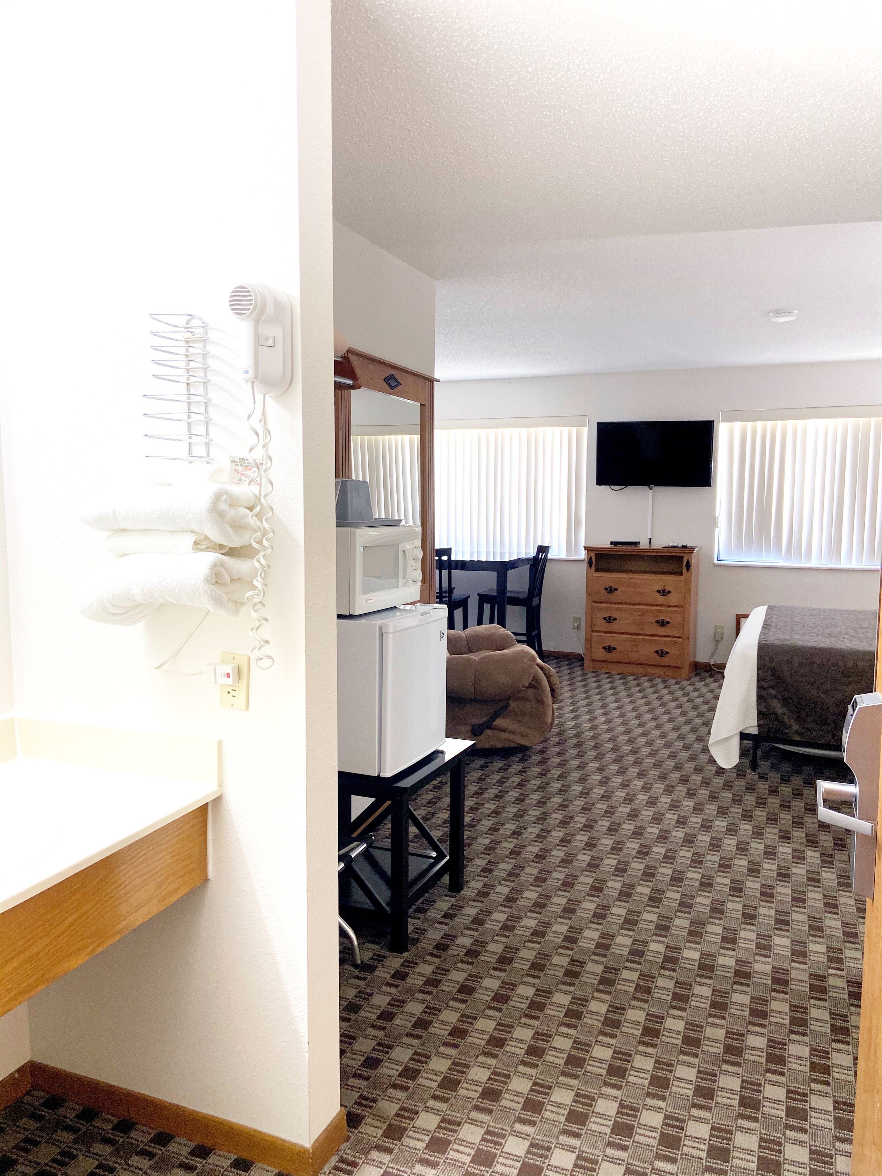 Quarto de hotel com cozinha compacta, televisão, cama e banheiro com porta-toalhas.