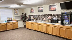 A well-lit kitchen with wooden cabinets, a microwave, a toaster, and a refrigerator. There are various food items and condiments on the counter, and a potted plant adds a touch of greenery. - Burke Inn Motel & Suites (Carroll)