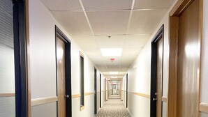 A hotel hallway with patterned carpet, wooden doors, and a ceiling with fluorescent lighting. - Burke Inn Motel & Suites (Carroll)