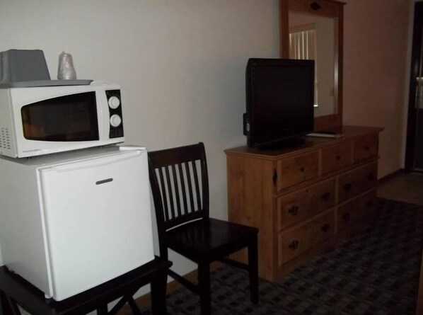 A compact kitchenette with a microwave, refrigerator, and a television on a wooden dresser.