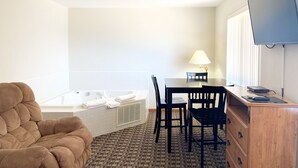 A room with a bathtub, a chair, a table with chairs, a lamp, a TV, and a wooden cabinet. - Burke Inn Motel & Suites (Carroll)