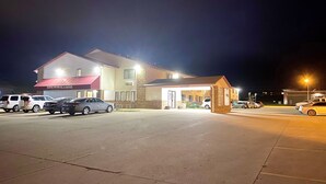 A motel with a red awning, a covered entrance, and several parked cars. - Burke Inn Motel & Suites (Carroll)