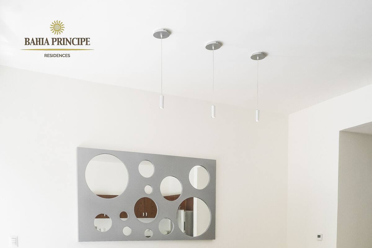 Ein modernes Wohnzimmer mit einem grauen Sofa, einem Glastisch und einem an der Wand befestigten abstrakten Kunstwerk.