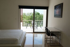 A bedroom with a bed, a desk, and a balcony with chairs and a table.