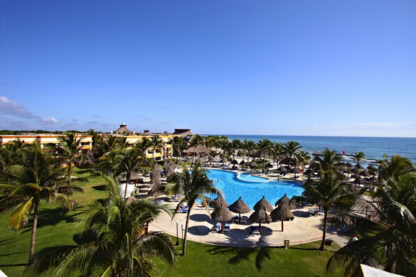 Un resort con una gran piscina, palmeras y sombrillas de playa.
