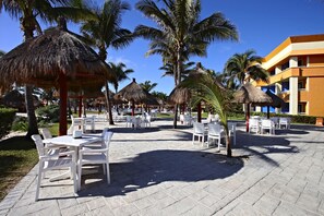 A resort with outdoor seating areas, palm trees, and thatched umbrellas.