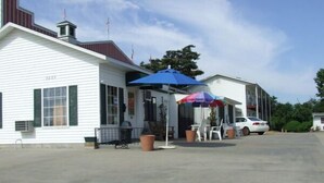 A white building with a covered outdoor seating area and a car parked in front. - The Skyline Motel (Osage Beach)