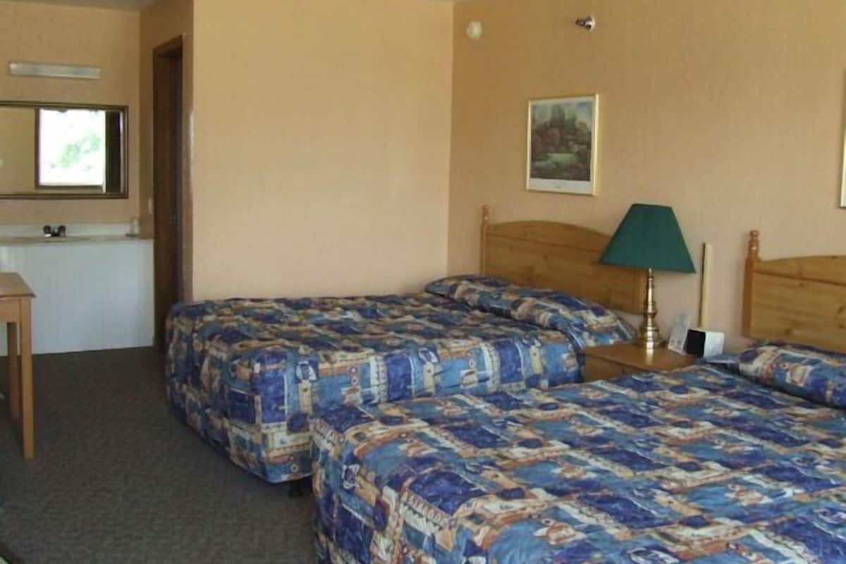 A hotel room with two beds, a desk, a chair, a lamp, and a painting on the wall.