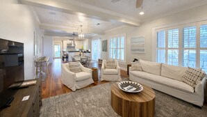 A spacious living room with a large sofa, two armchairs, a coffee table, and a TV. There is a kitchen in the background with a dining area. - Bay Town Inn (Bay St Louis)
