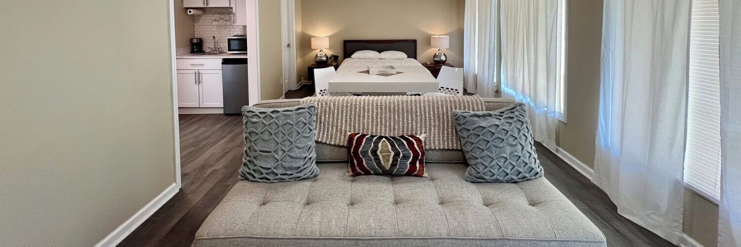 Une chambre d’hôtel comprenant un lit, des tables de chevet, un petit coin salon avec des coussins et une vue sur l’extérieur.