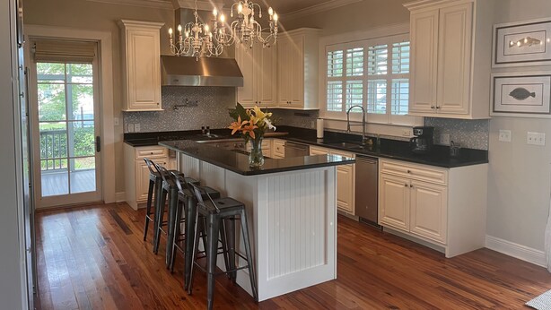 A spacious kitchen with a large island, white cabinetry, a stainless steel range hood, and a chandelier. - Bay Town Inn (Bay St Louis)