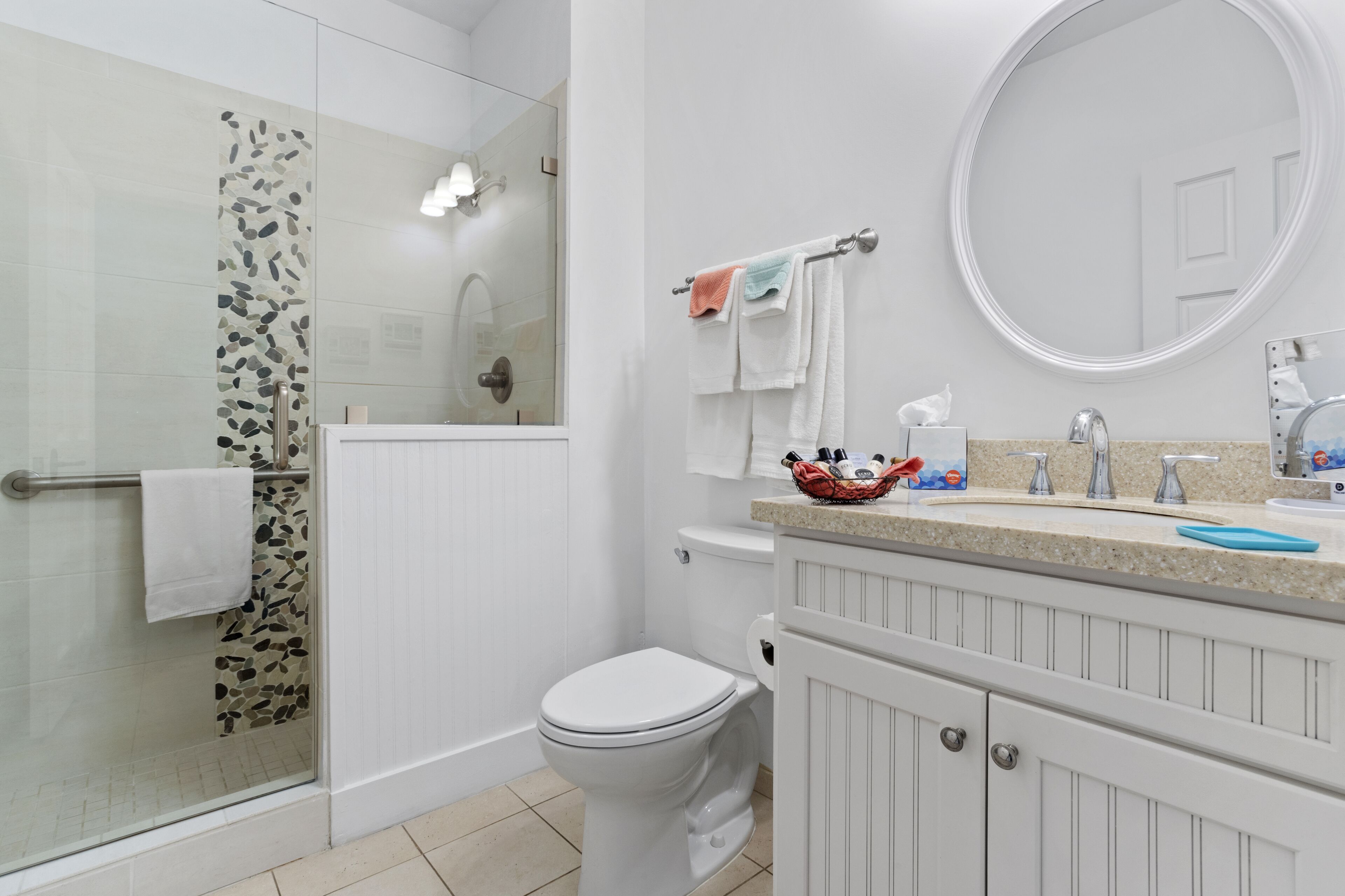 A bathroom with a glass shower enclosure, a toilet, a sink with a mirror, and a towel rack.