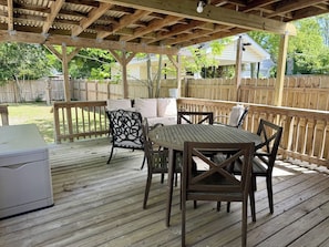 A wooden deck with a table and chairs, a covered seating area, and a wooden fence in the background.