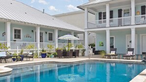 A pool area with lounge chairs and umbrellas, a covered patio, and a two-story building with balconies. - Bay Town Inn (Bay St Louis)