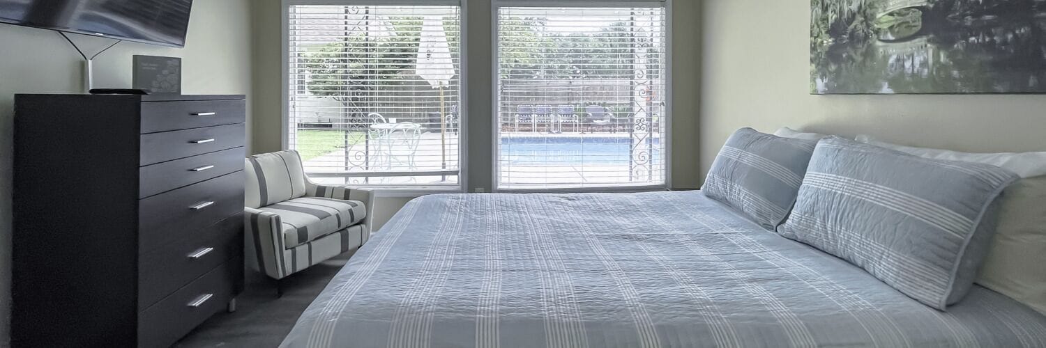 A bedroom with a bed, a dresser, a chair, and a window with blinds.