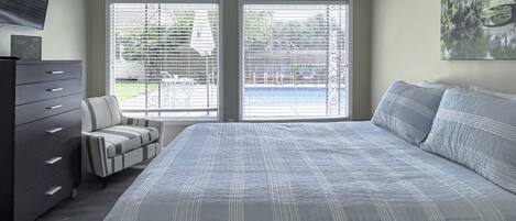 A bedroom with a bed, a dresser, a chair, and a window with blinds.