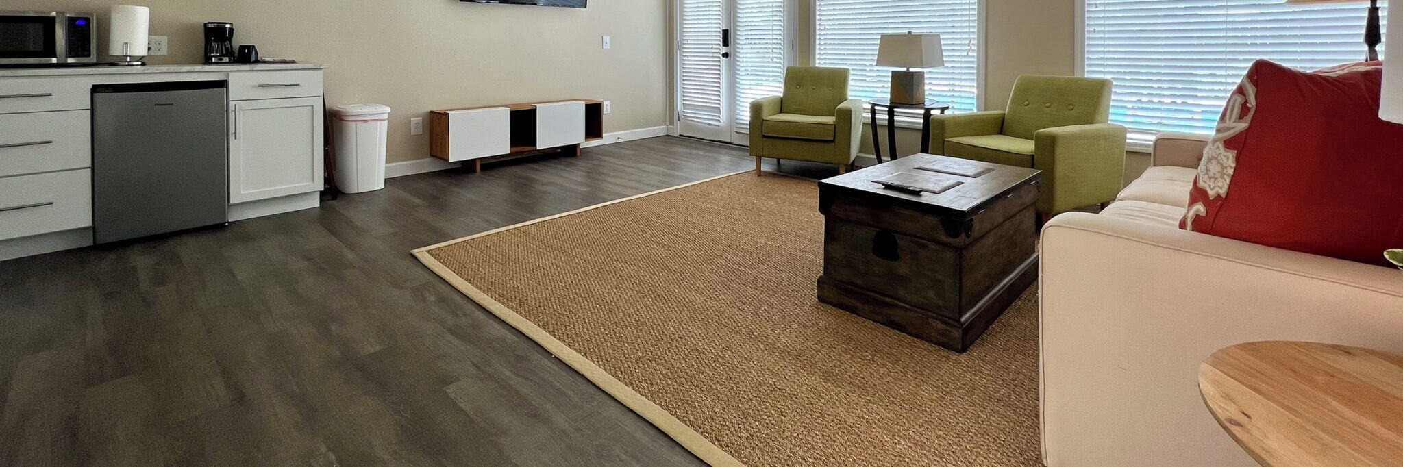 Un salon moderne comprenant un canapé, deux fauteuils, une table basse et un coin cuisine avec un lave-vaisselle, ainsi qu'une poubelle.